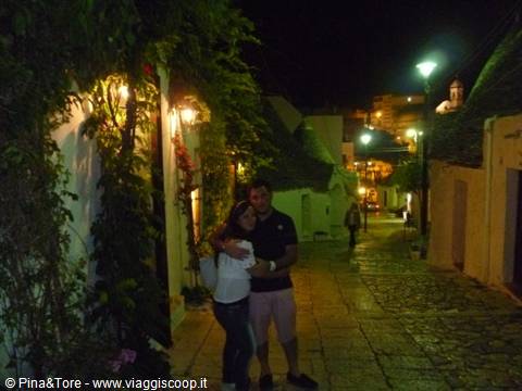 Couple embracing at night among Alberobello trulli, lantern-lit stone streets