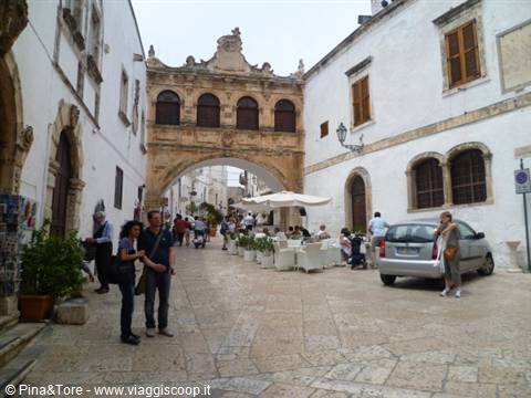Stone arch over the street, whitewashed buildings and tourists in Ostuni