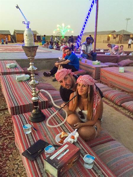 Couple in keffiyeh next to a shisha pipe on desert camp cushions