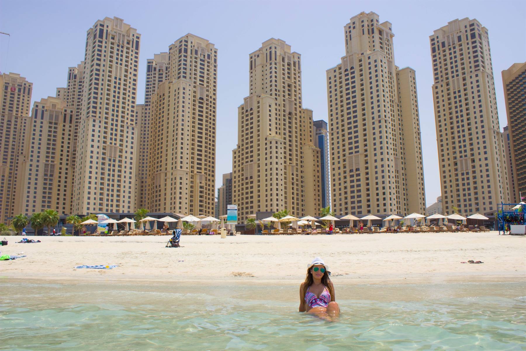 Donna seduta in acqua turchese sulla spiaggia di JBR, grattacieli alle spalle
