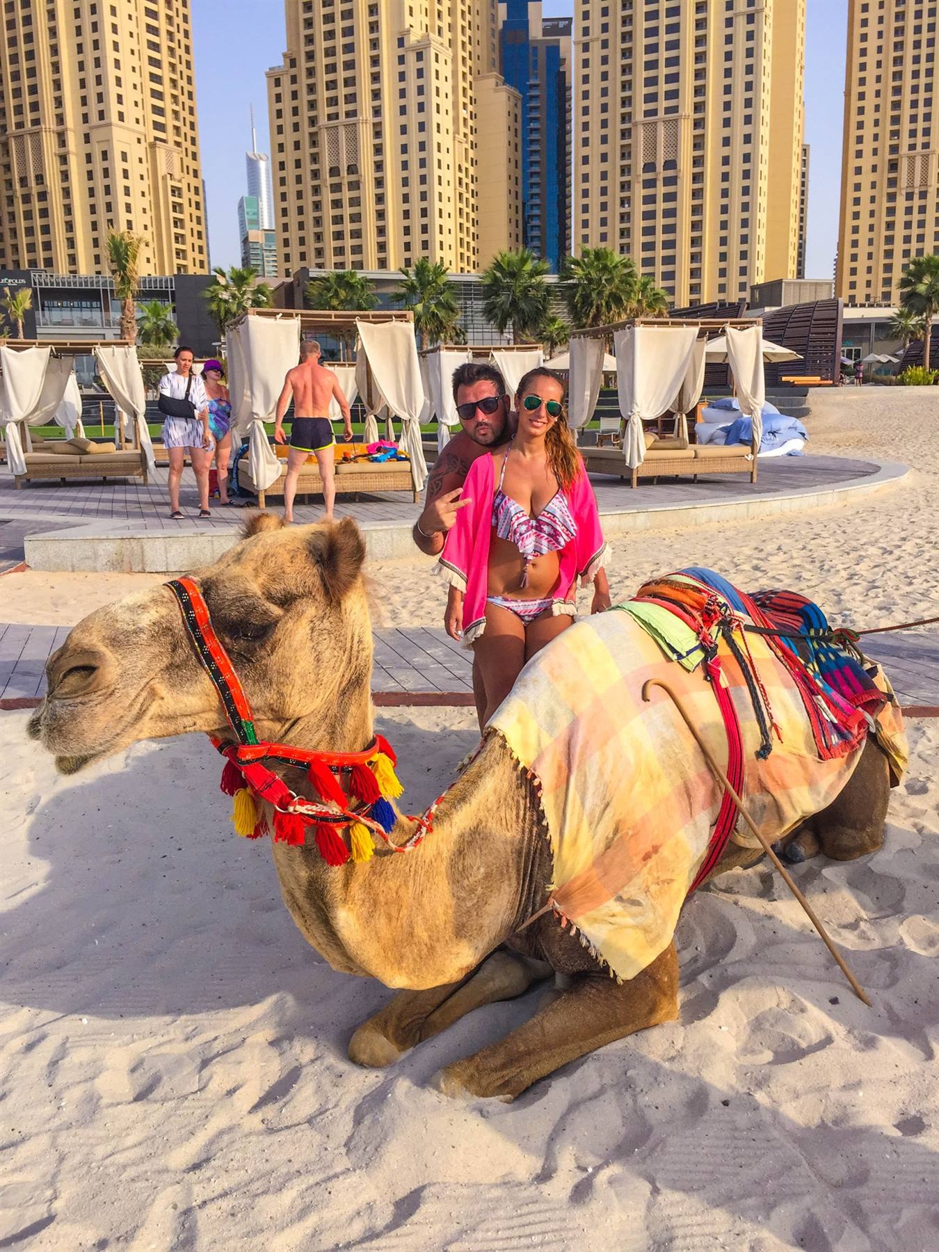 Coppia con cammello in sella colorata sulla spiaggia di Dubai Marina
