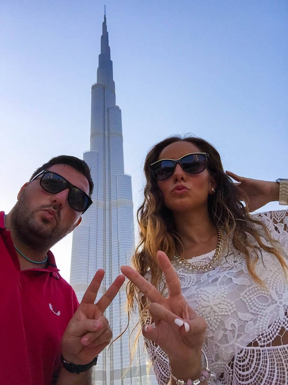 Due giovani con occhiali fanno peace al Burj Khalifa, luce solare
