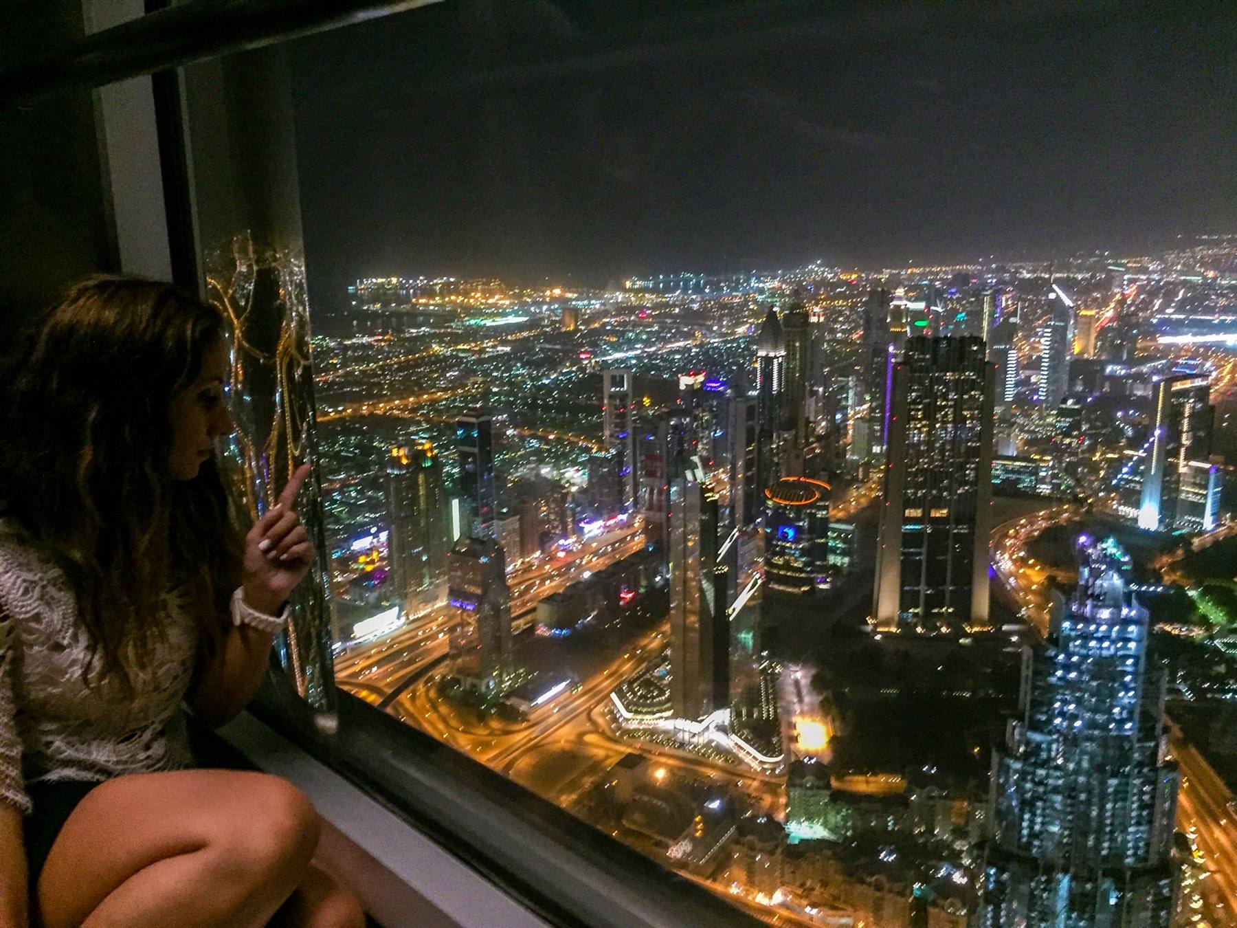 Ragazza al Burj Khalifa indica i grattacieli illuminati di Dubai di notte