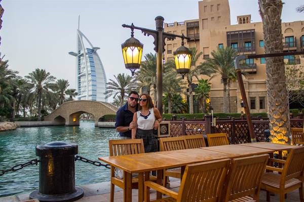 Couple by wooden tables, Burj Al Arab and bridge over the waterway