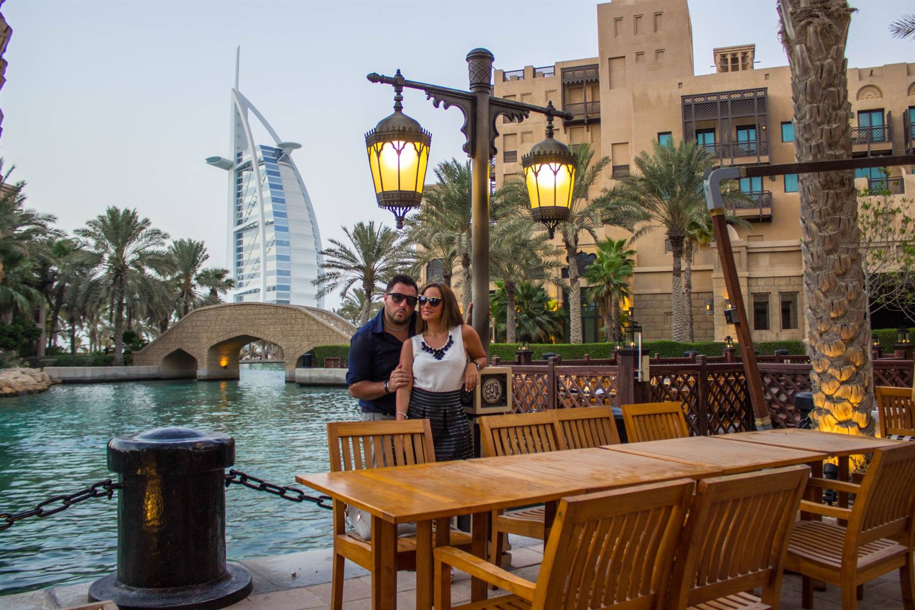 Coppia accanto a tavoli di legno, Burj Al Arab e ponte sul canale d'acqua