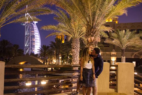 Couple kissing among palm trees at night, Burj Al Arab lit behind