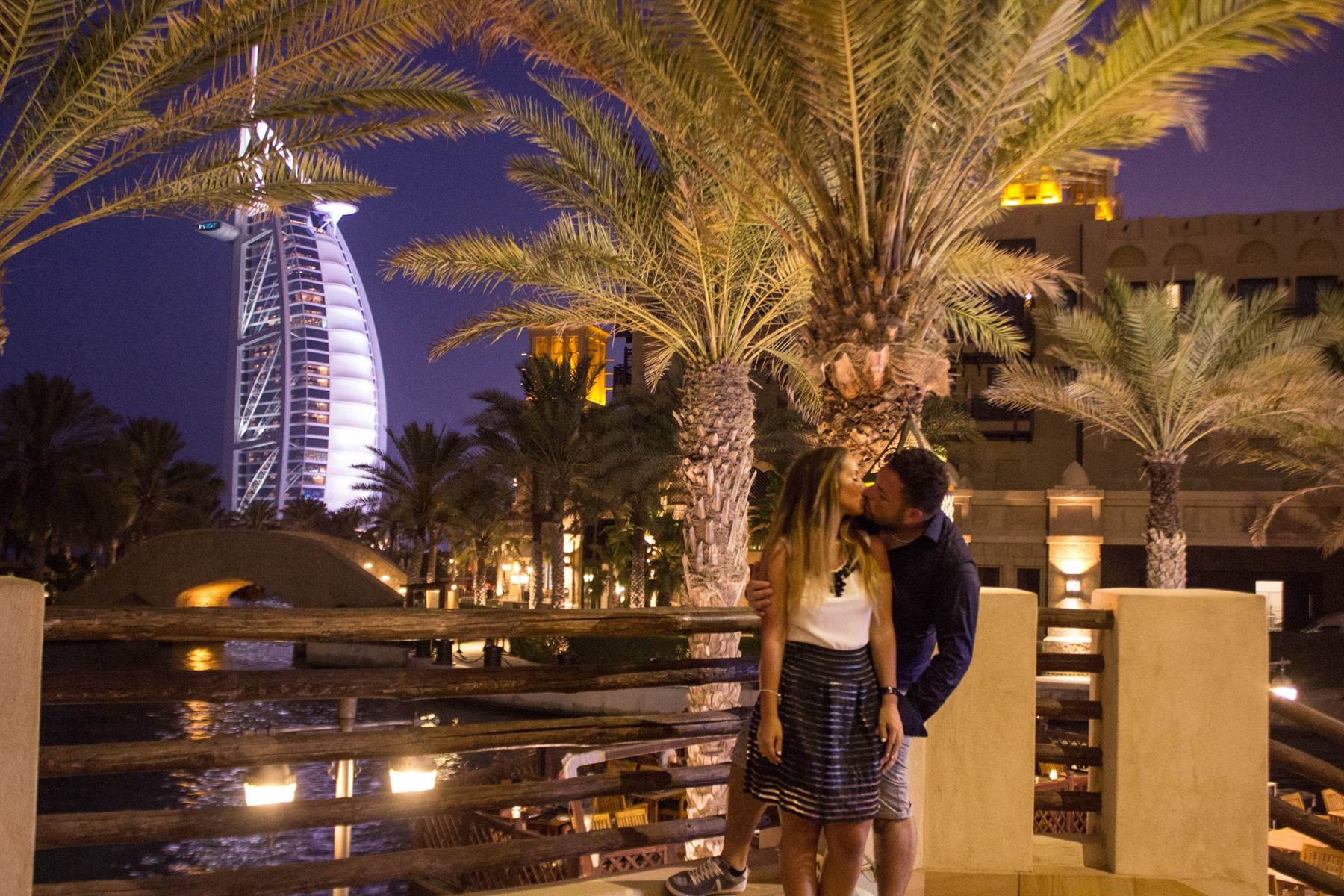 Coppia si bacia tra palme di notte, Burj Al Arab illuminato sullo sfondo