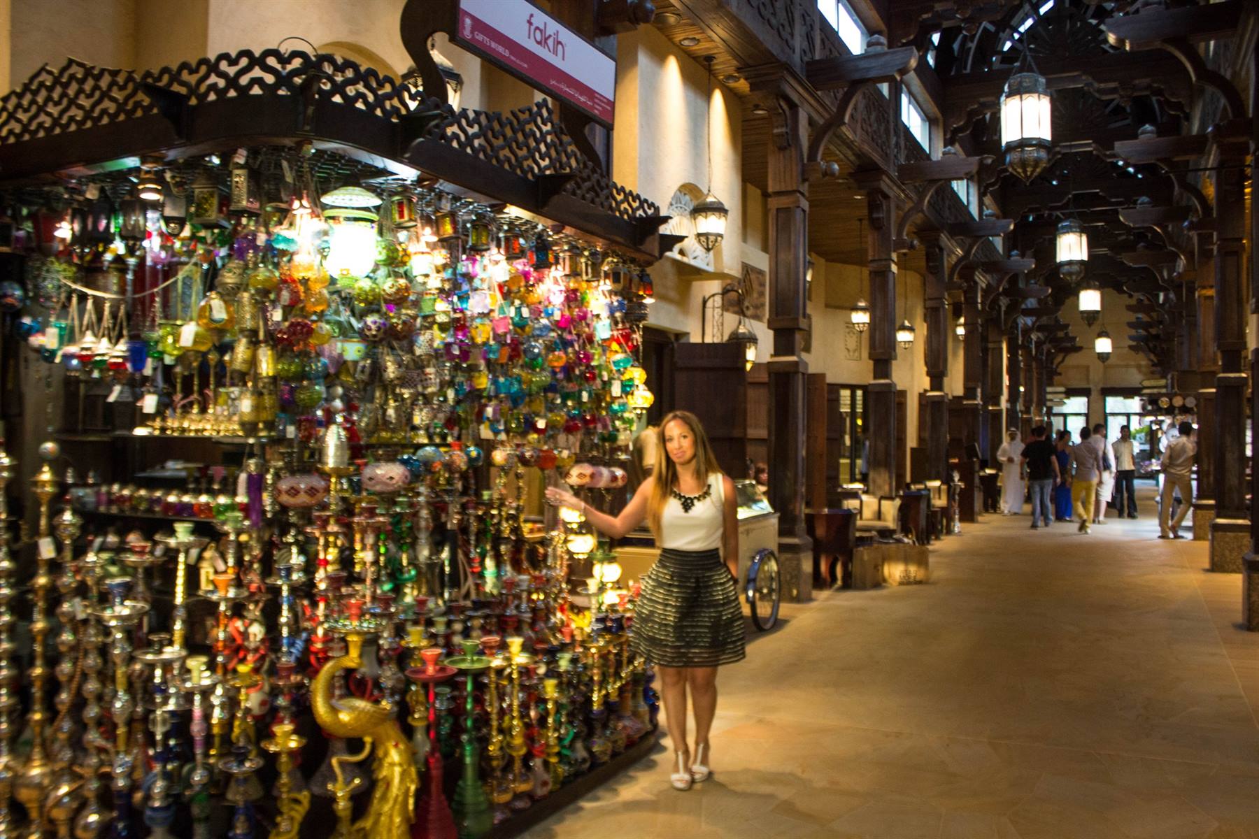 Donna accanto a un banco di lanterne colorate e narghilé in un souk coperto di legno