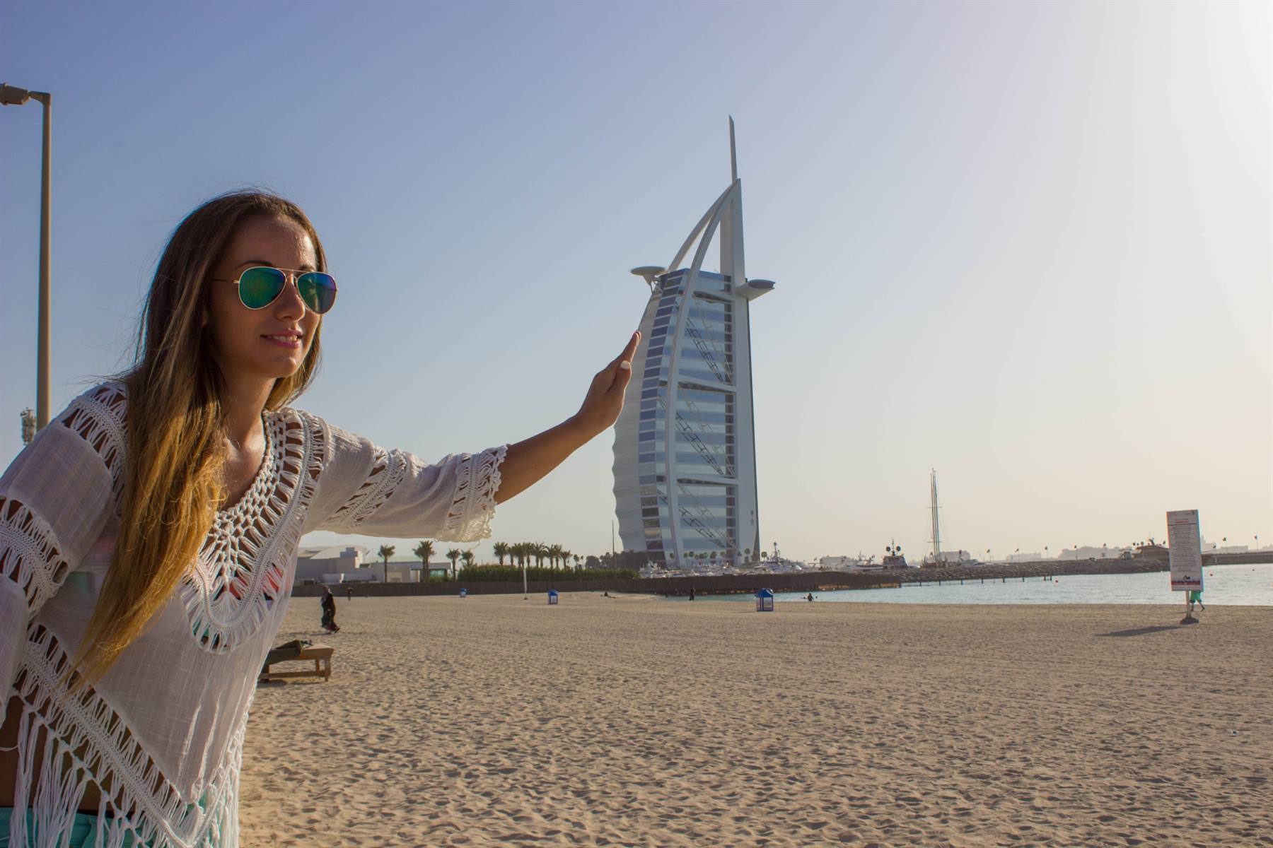 Turista con occhiali sfiora con la mano il Burj Al Arab dalla spiaggia