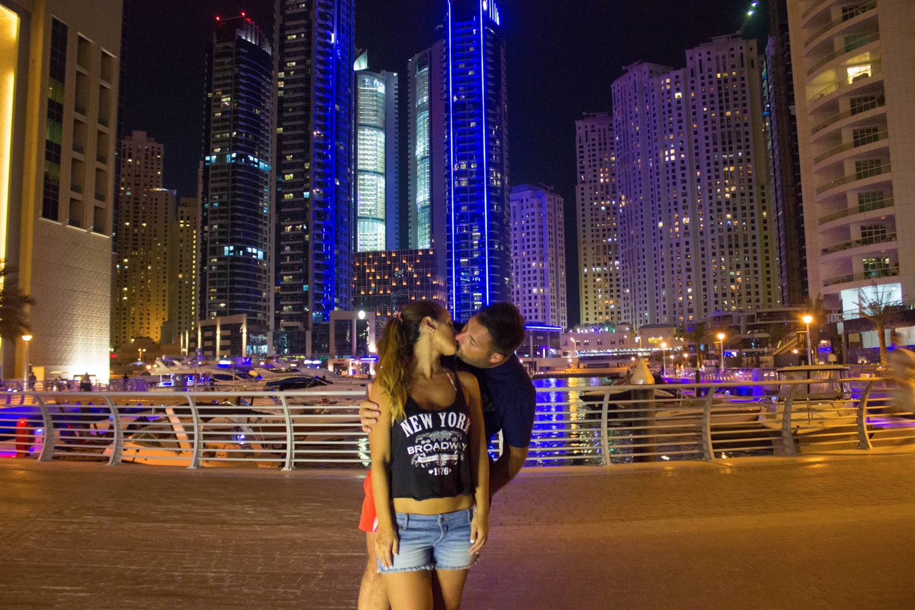 Coppia che si bacia di notte a Dubai Marina tra grattacieli illuminati di blu