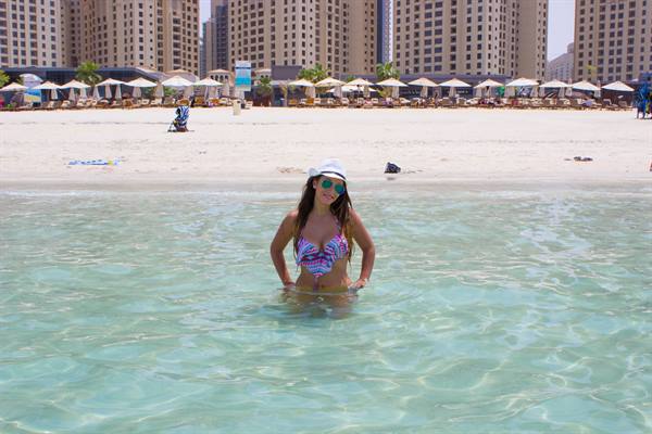 Woman in white hat in turquoise sea, beach with umbrellas and skyscrapers behind