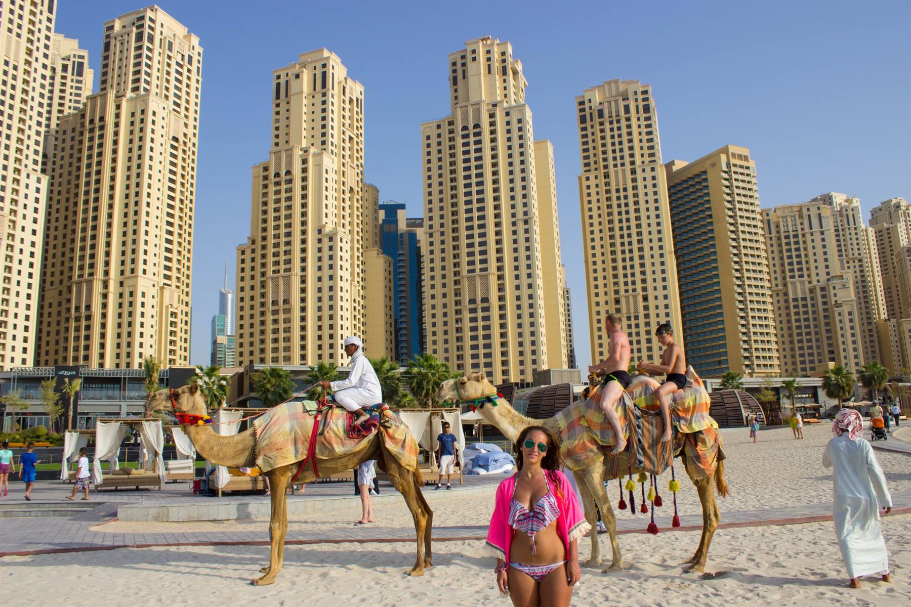 Turisti su cammello in spiaggia tra i grattacieli di Dubai Marina