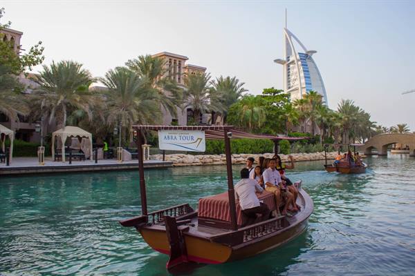 Tourists on a traditional wooden abra boat at Madinat Jumeirah, Burj Al Arab behind