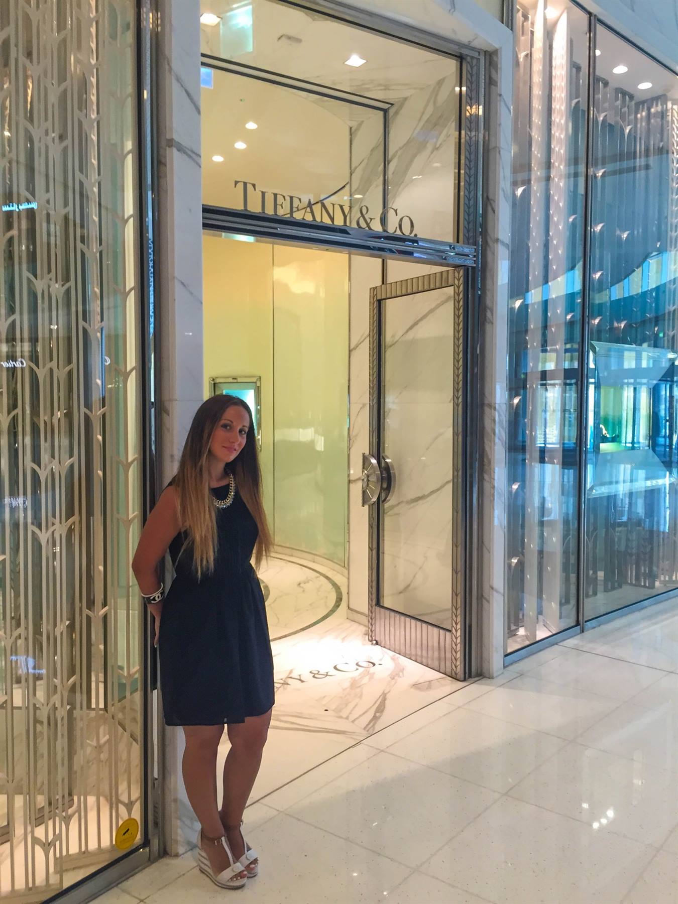 Donna in vestito blu davanti all'ingresso Tiffany & Co in marmo