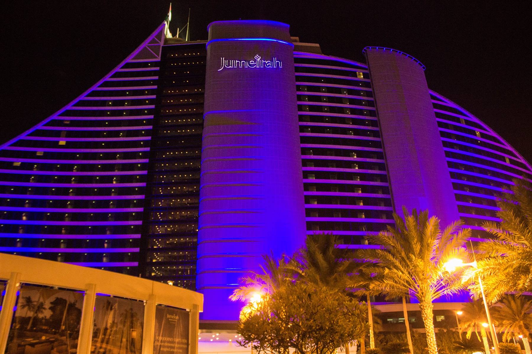 Hotel Jumeirah illuminato di viola di notte, palme e lampioni davanti