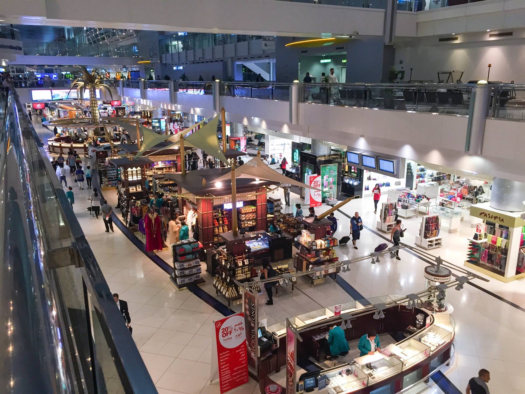 Terminal dell'aeroporto di Dubai con negozi, chioschi e viaggiatori tra luci artificiali