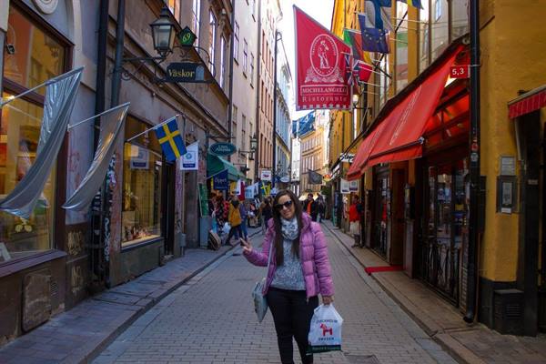 Tourist in pink down jacket waves on a cobbled Gamla Stan street, Stockholm