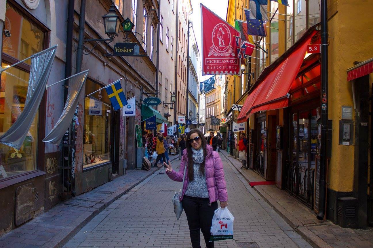 Turista con piumino rosa saluta in un vicolo lastricato di Gamla Stan, Stoccolma