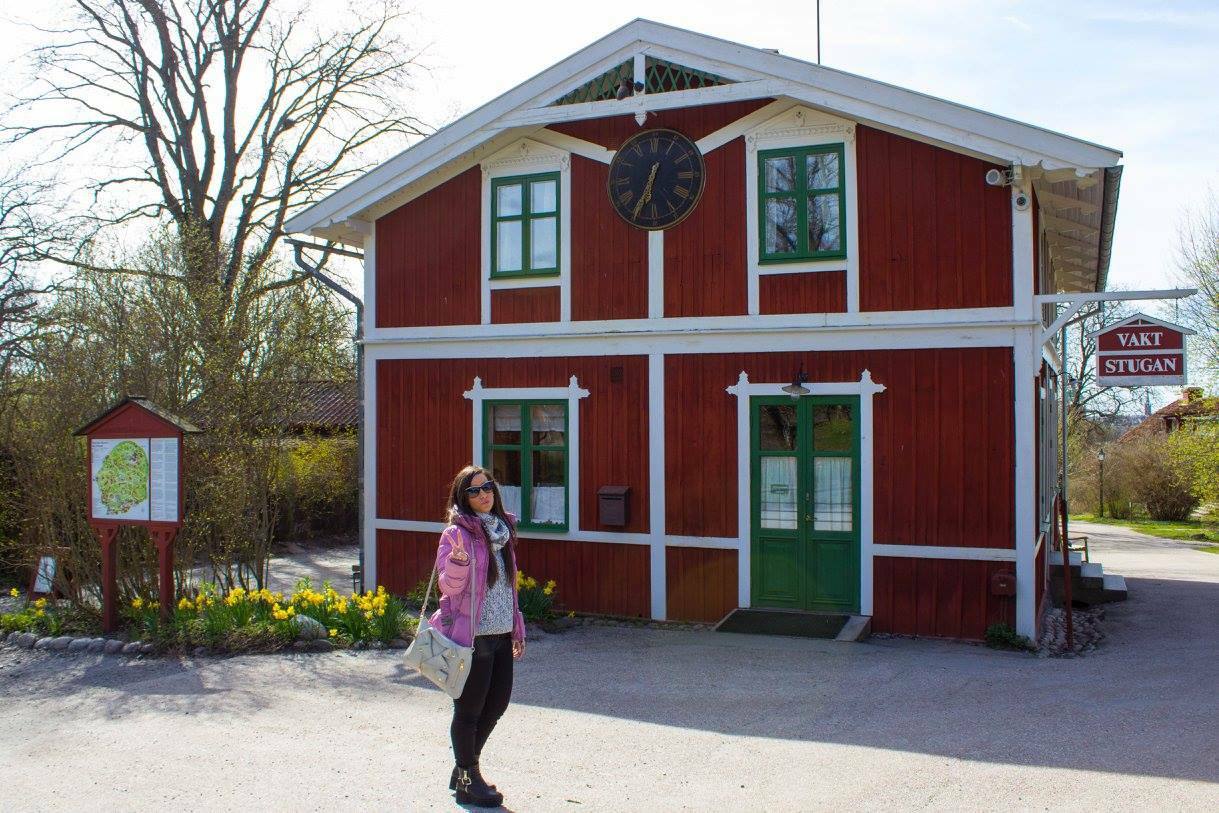 Turista davanti a una casa di legno rossa con orologio e insegna Yalm Stugan