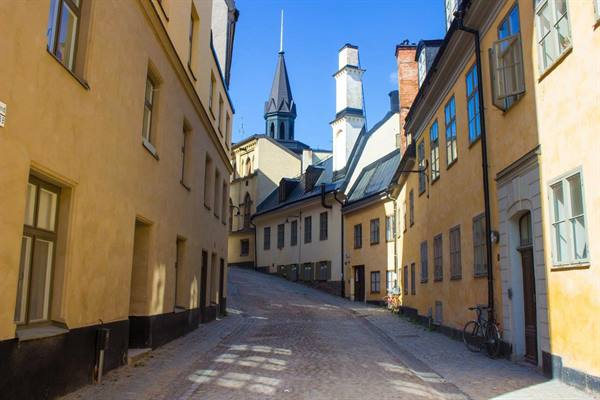 Cobbled alley in Gamla Stan, Stockholm, yellow facades and spire in sunlight