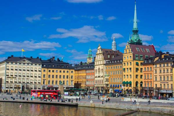Colorful buildings along Stockholm's Gamla Stan waterfront, tourists and red buses