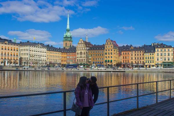 Couple kissing by the waterfront in front of Gamla Stan's colorful buildings, Stockholm