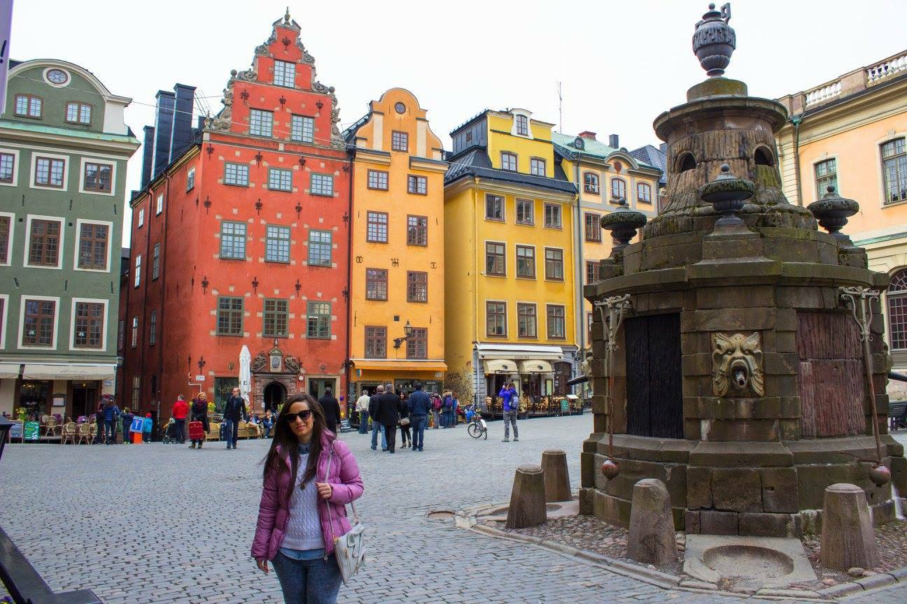 Turista in giacca rosa davanti alla fontana in pietra di Stortorget, Stoccolma