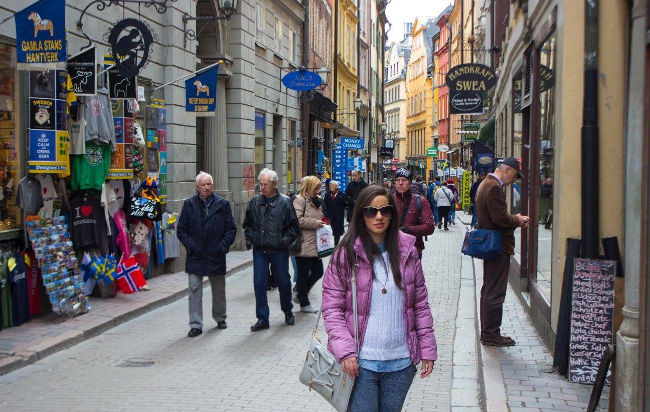 Donna con giacca rosa cammina in una via pedonale affollata di negozi, Gamla Stan, Stoccolma