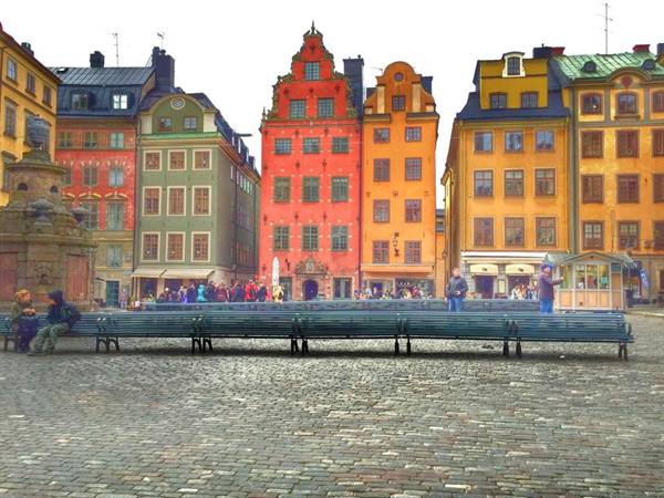 Green benches on cobblestones in front of colorful houses at Stortorget, Stockholm