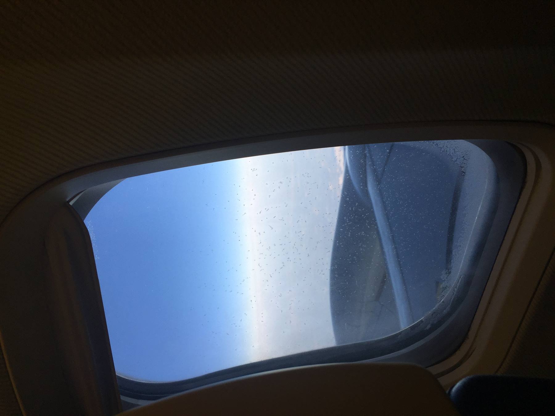 Finestrino dell'aereo con gocce d'acqua e ala bagnata sotto cielo azzurro
