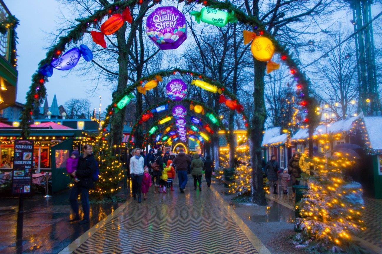 Arcate illuminate con dolciumi Quality Street al Tivoli di Copenaghen, visitatori sotto gli alberi natalizi