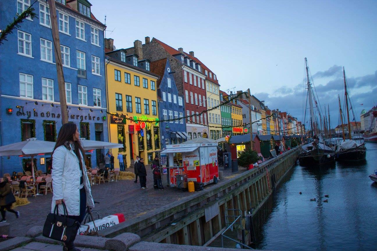 Donna in cappotto bianco cammina lungo i casecolorati di Nyhavn con barche attraccate