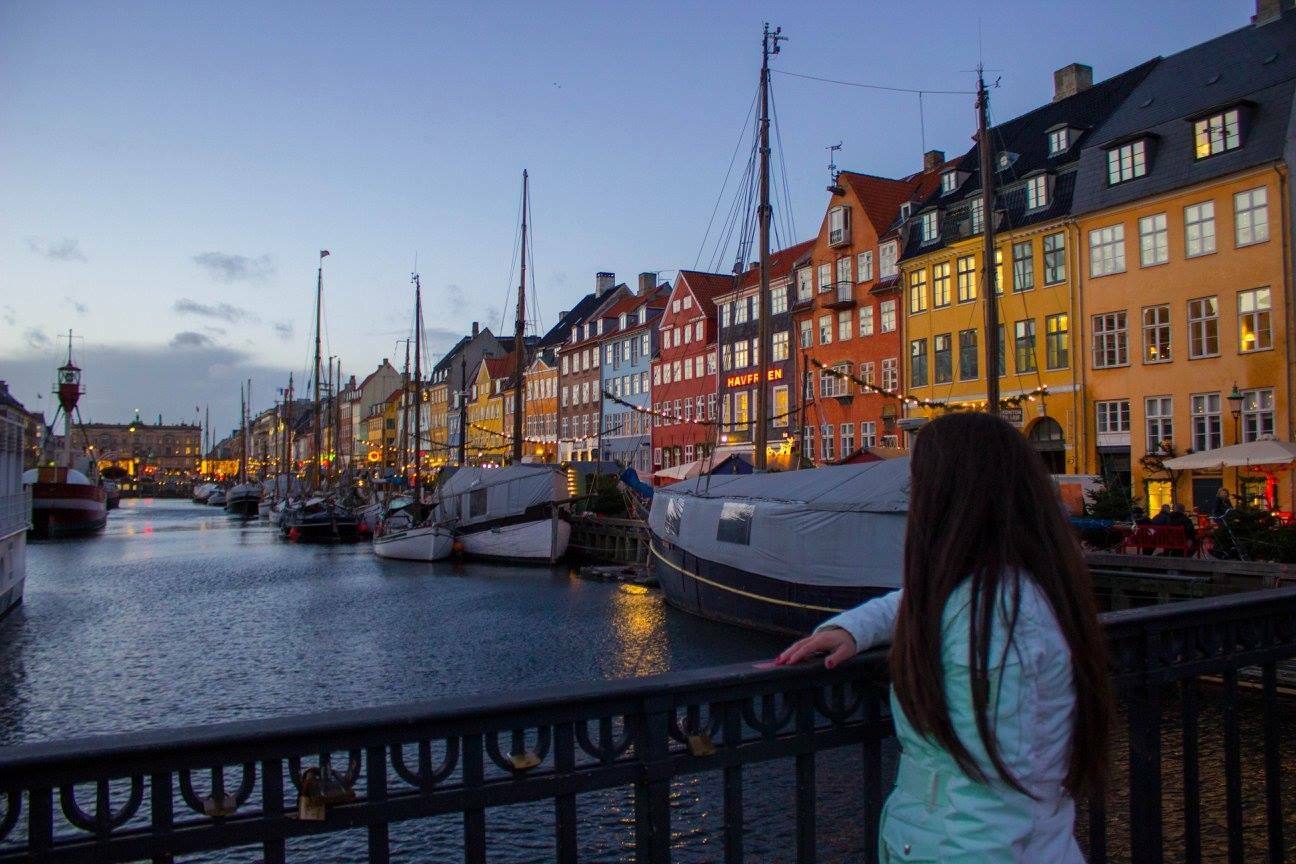 Ragazza su un ponte guarda le case colorate e le barche di Nyhavn a Copenaghen