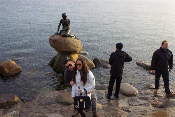 Tourists in front of Copenhagen's Little Mermaid, bronze statue on rocks by the water
