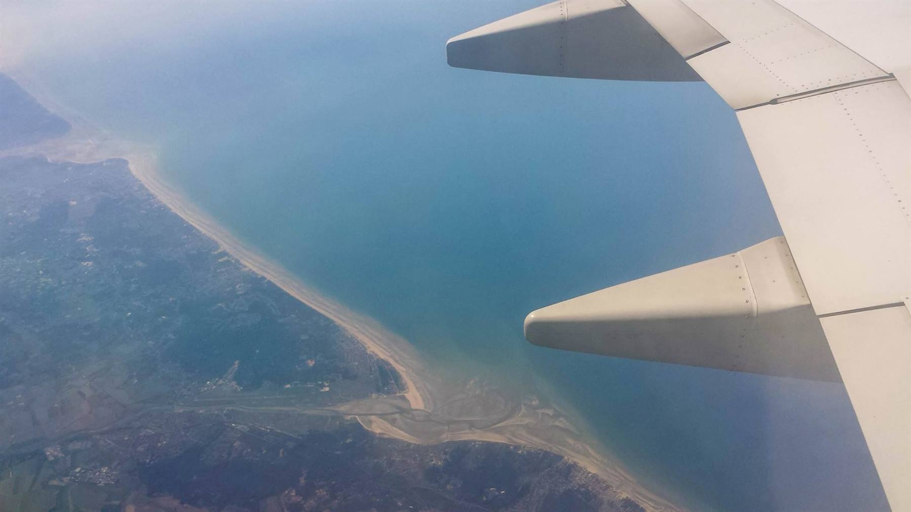 L'ala dell'aereo sopra una lunga spiaggia sabbiosa e il mare turchese