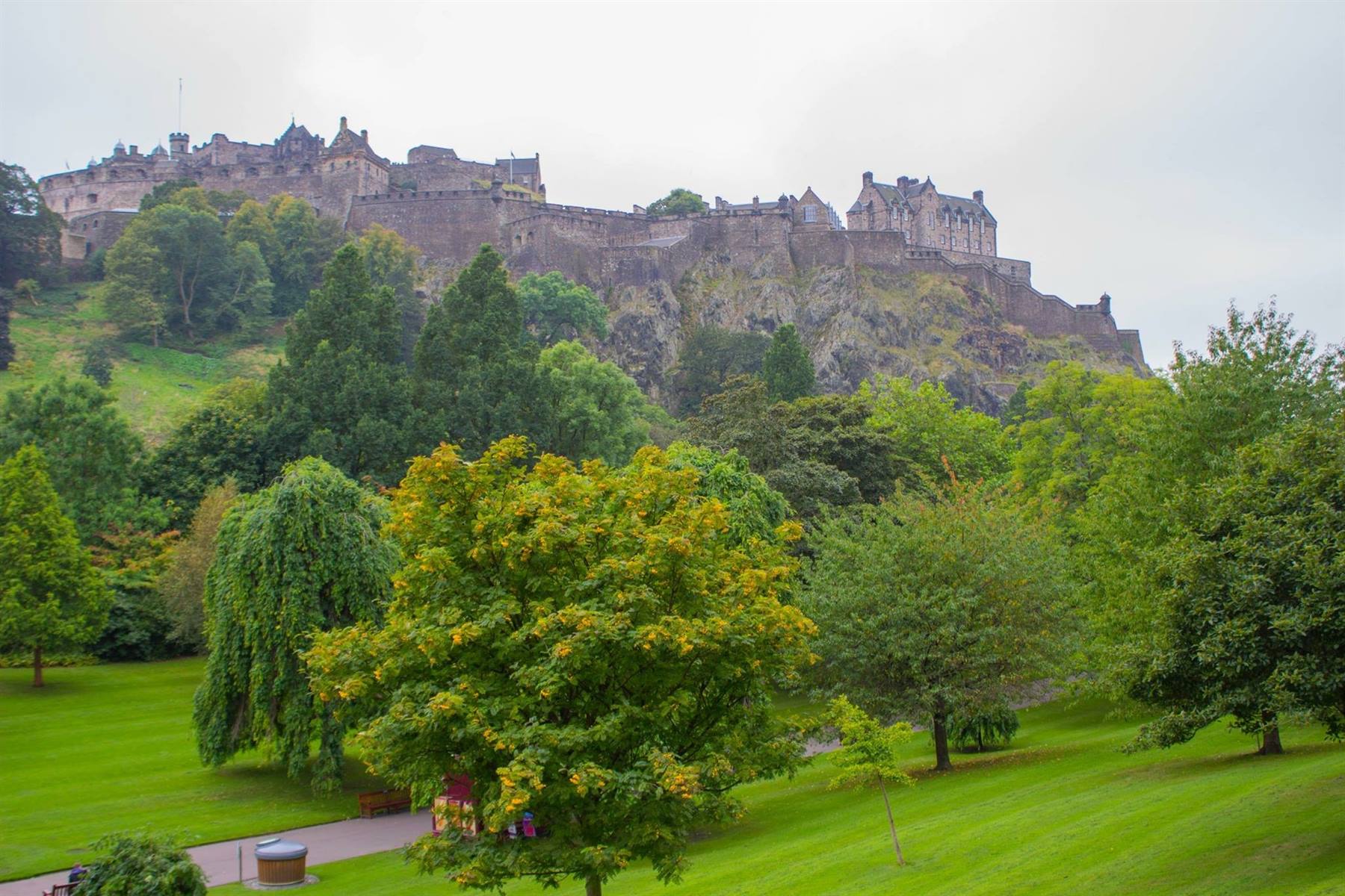 Il Castello di Edimburgo su una roccia, circondato da alberi verdeggianti sotto cielo grigio