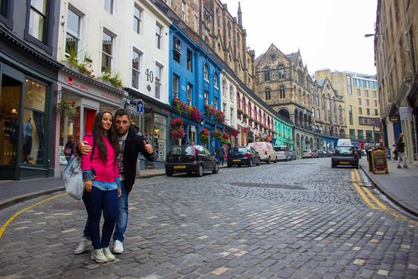 Couple posing on Victoria Street, Edinburgh, among colorful shopfronts and cobblestones