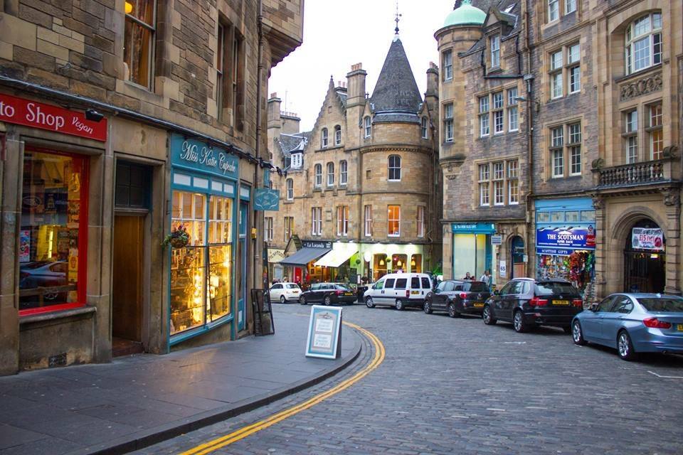 Cockburn Street a Edimburgo, edifici in pietra, negozi illuminati e auto parcheggiate