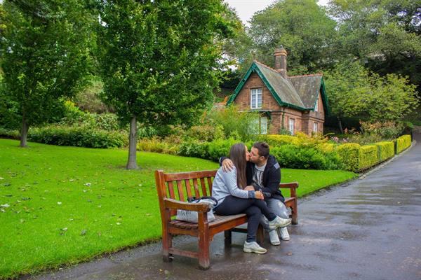 Couple embracing on a wooden bench in front of a brick park cottage