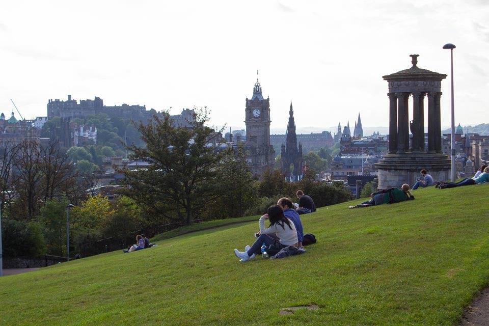 Turisti seduti sull'erba di Calton Hill, Edimburgo, col monumento di Dugald Stewart