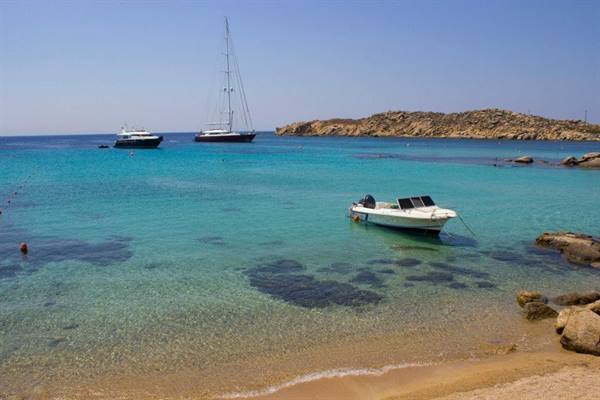 Boats anchored in turquoise bay, golden rocks and pale sand under blue sky
