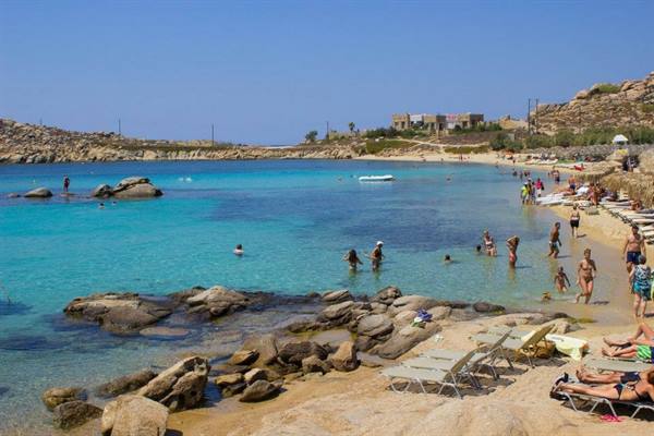 Swimmers in turquoise water among rocks, sunbeds and umbrellas on Paranga beach