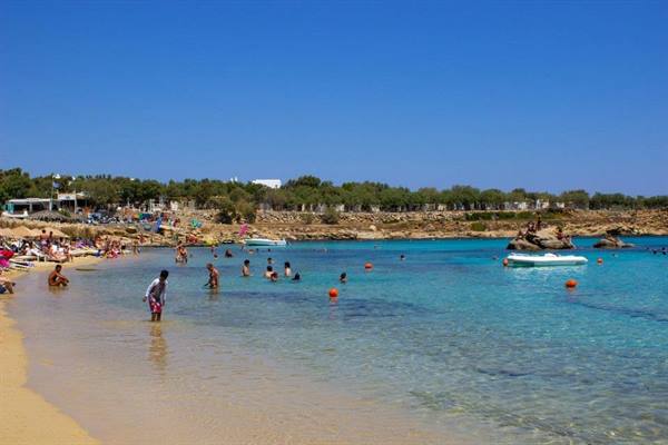 Swimmers in turquoise water at Paraga Beach, motorboats anchored and golden sand