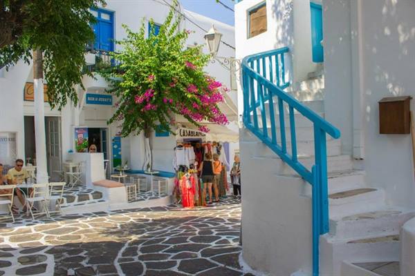 Whitewashed alley with turquoise staircase, blooming bougainvillea and tourists near shops
