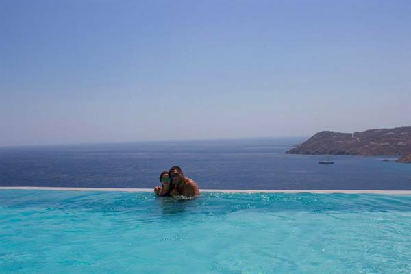 Couple in turquoise infinity pool water facing the sea and rocky coastline