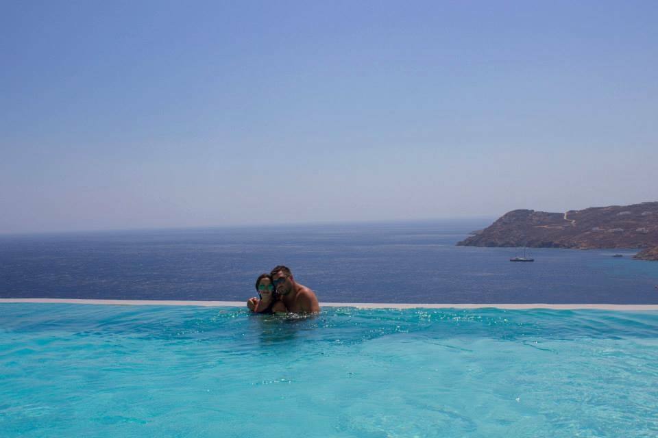 Coppia nell'acqua turchese di una piscina infinita davanti al mare e scogliera