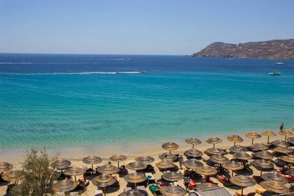 Beach with straw umbrellas, turquoise sea, boats and arid headland, Mykonos