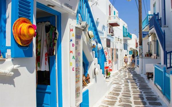 Mykonos alley with white shops and blue doors, tourists walk past staircases