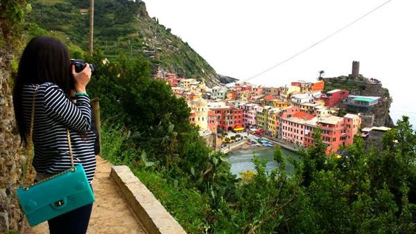 Woman with turquoise bag photographs Vernazza's colorful houses from the hillside