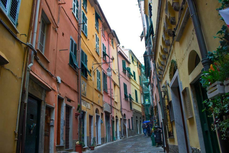 Vicolo stretto tra case colorate con persiane verdi, ciottoli bagnati, passanti a Monterosso